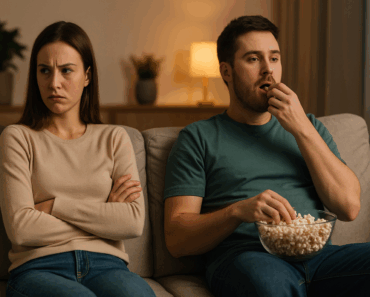 “A passive-aggressive couple on a couch illustrating emotional disengagement in modern relationships — satirical visual for MediaBreakfast.club article on ‘mankeeping’.”